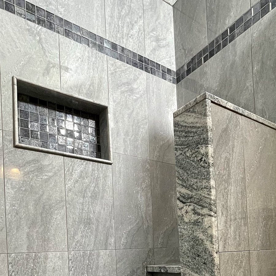 Close-up of a tiled shower wall with a mosaic band and niche